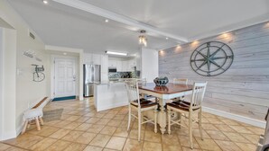 A spacious kitchen with white cabinetry, a central island, and a dining area with a wooden table and chairs. - Dolphin Point 502b (Destin)