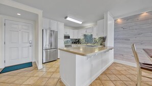 A modern kitchen with white cabinetry, a stainless steel refrigerator, a built-in island with a granite countertop, and a backsplash with blue tiles. - Dolphin Point 502b (Destin)
