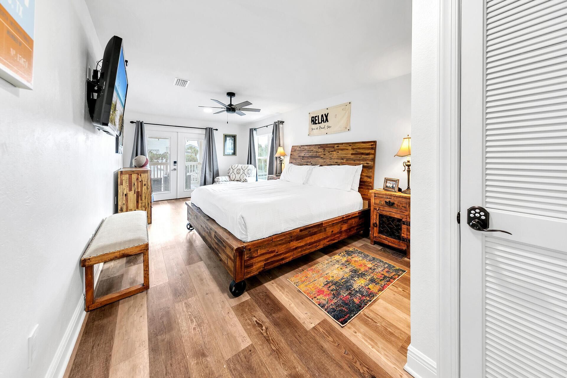 A bedroom with a wooden bed, a ceiling fan, a TV mounted on the wall, and a 'RELAX' sign.
