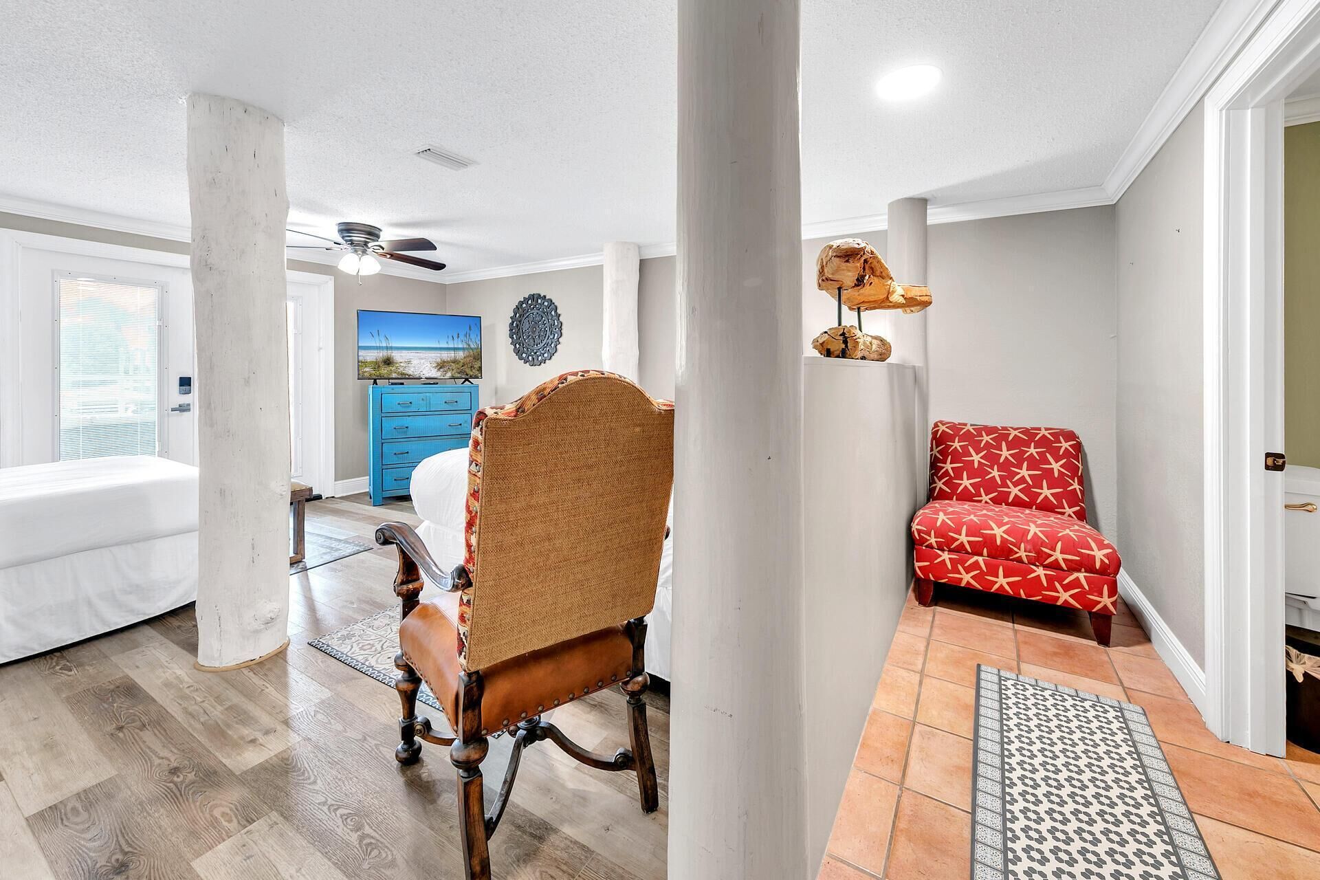 A spacious living room with a large window, a blue cabinet, a wicker chair, a red sofa, and a ceiling fan.