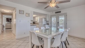 A modern kitchen with white cabinets, a glass dining table, and a ceiling fan. - The Back Porch (Destin)