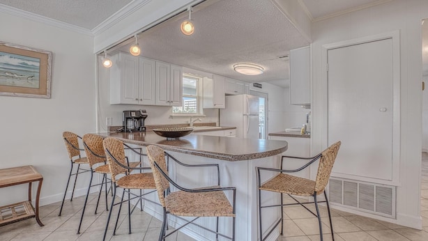 A kitchen with a central island, bar stools, and a coffee maker. - The Back Porch (Destin)