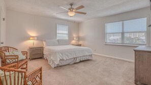 A bedroom with a bed, two nightstands, a ceiling fan, and two windows with blinds. - The Back Porch (Destin)