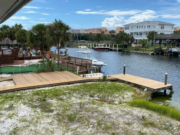 A marina with boats docked, a wooden deck, and a view of buildings in the background. - The Back Porch (Destin)