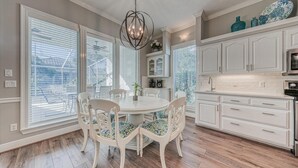 Una cocina con muebles blancos, una mesa redonda con sillas y una araña.