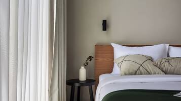 Quarto de hotel com uma cama, uma mesa de cabeceira, um vaso com planta e cortinas translúcidas.
