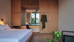 Een moderne hotelkamer met een bed, een bureau, een kledingkast en een groot raam met uitzicht op groen.