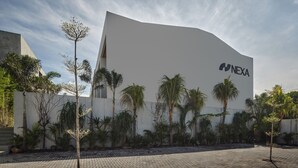 Een modern gebouw met een witte gevel en het logo 'NEXA', omringd door palmbomen en een verhard gebied.