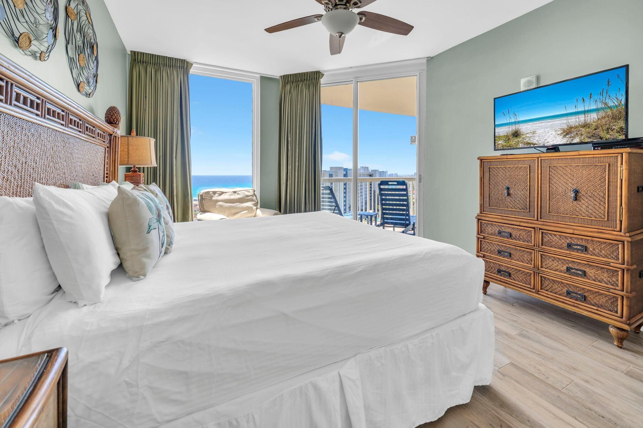 Un dormitorio con una cama grande, televisor, cómoda de madera y vista a la playa.