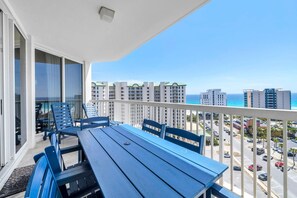 Balkon med bord og stole, udsigt over parkeringsplads og bygninger med kig til havet.