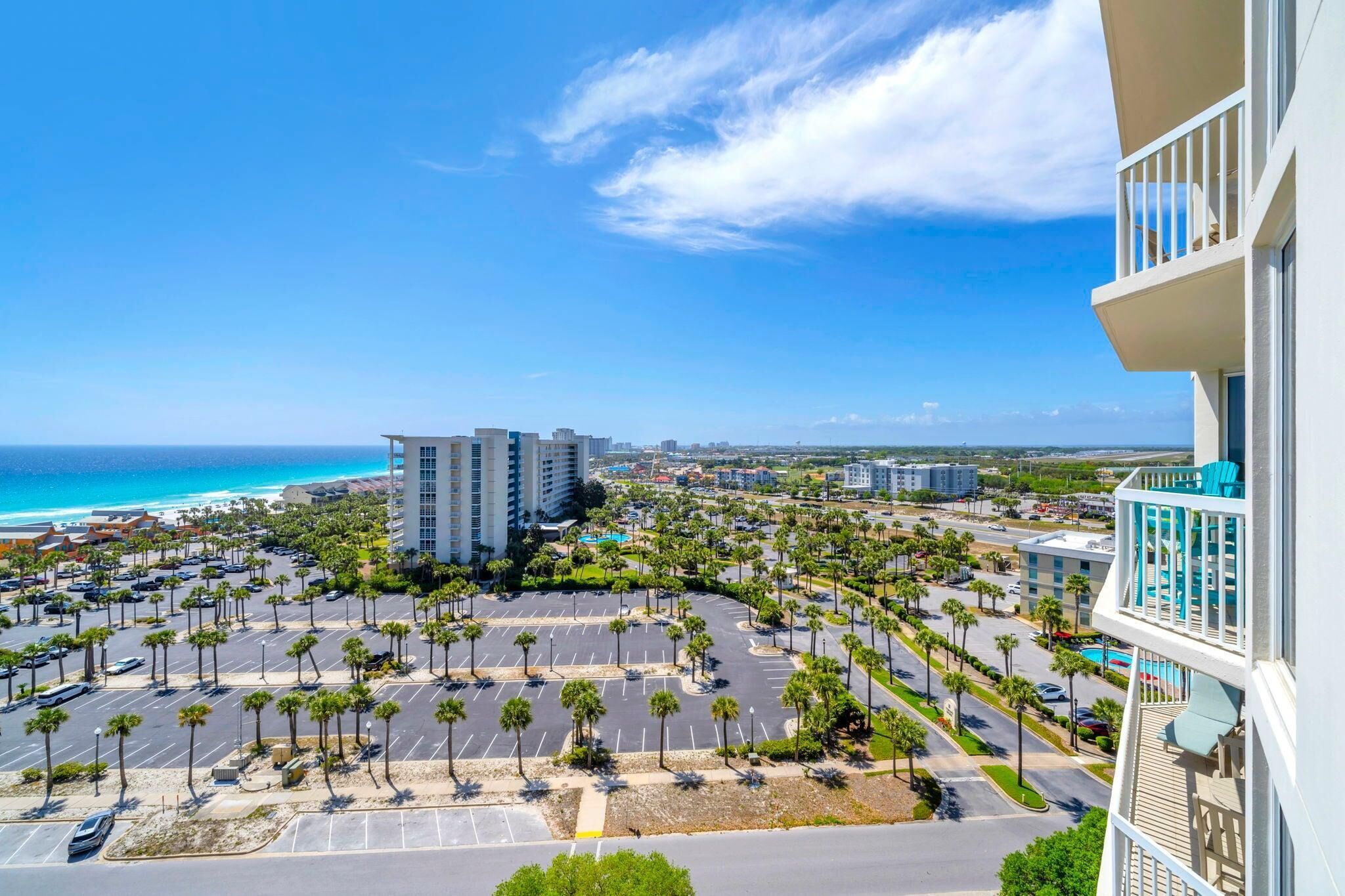 A high-rise hotel with a view of the ocean and a parking lot with palm trees.