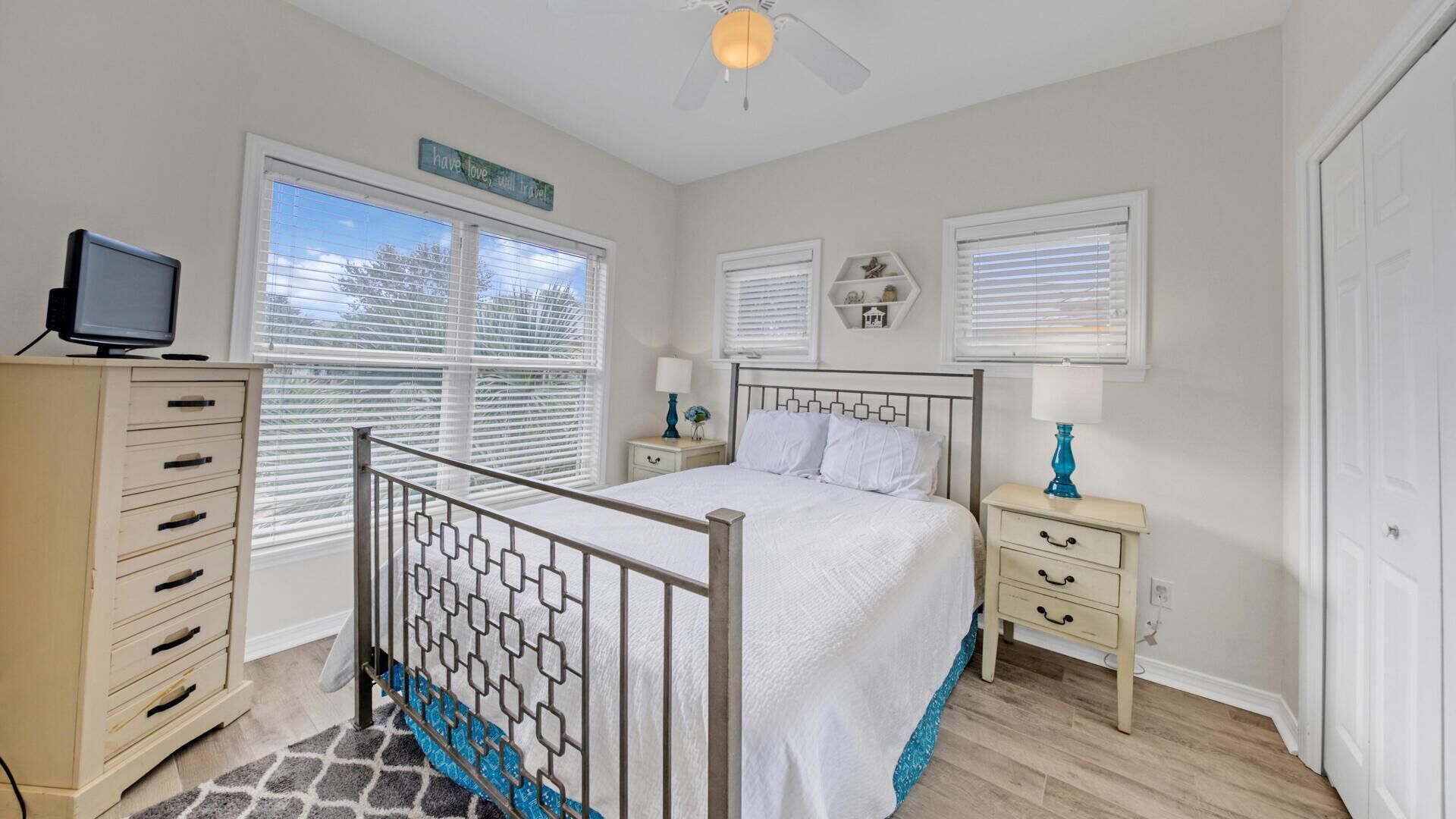 A bedroom with a bed, a dresser, a nightstand, a television, and a window with blinds.