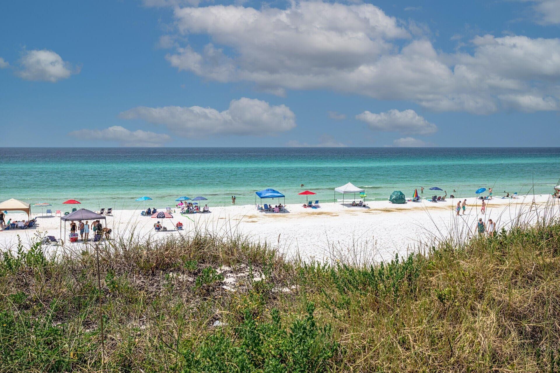 A beach with white sand, clear turquoise water, and several beach umbrellas.