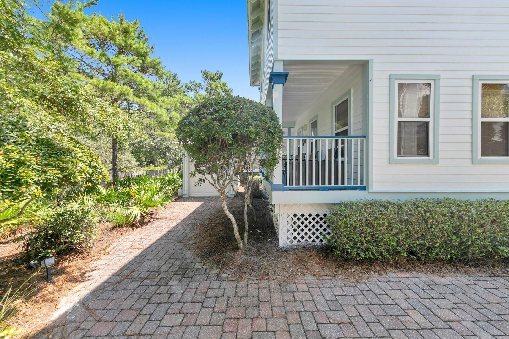 A house with a covered porch, a brick pathway, and surrounding greenery.