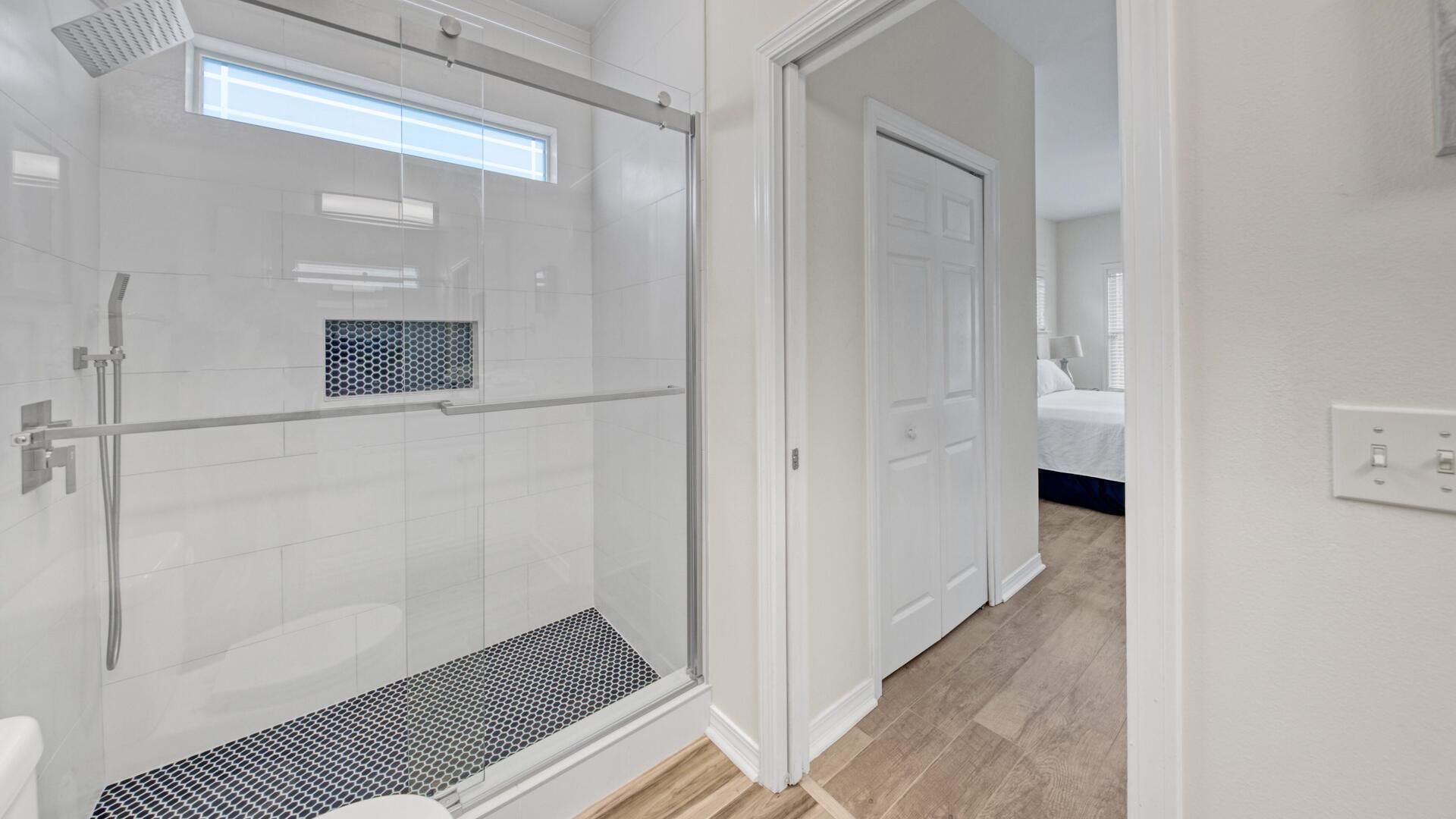Une salle de bain moderne avec une douche à l’italienne en verre, des toilettes et une pomme de douche visible.