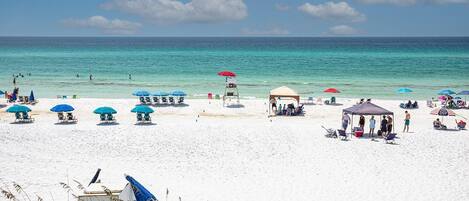 A beach with white sand, clear turquoise water, and several beach umbrellas and lounge chairs.