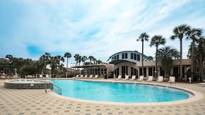 A swimming pool with lounge chairs and palm trees, surrounded by a building with a curved roof. - Destiny Casa (Destin)