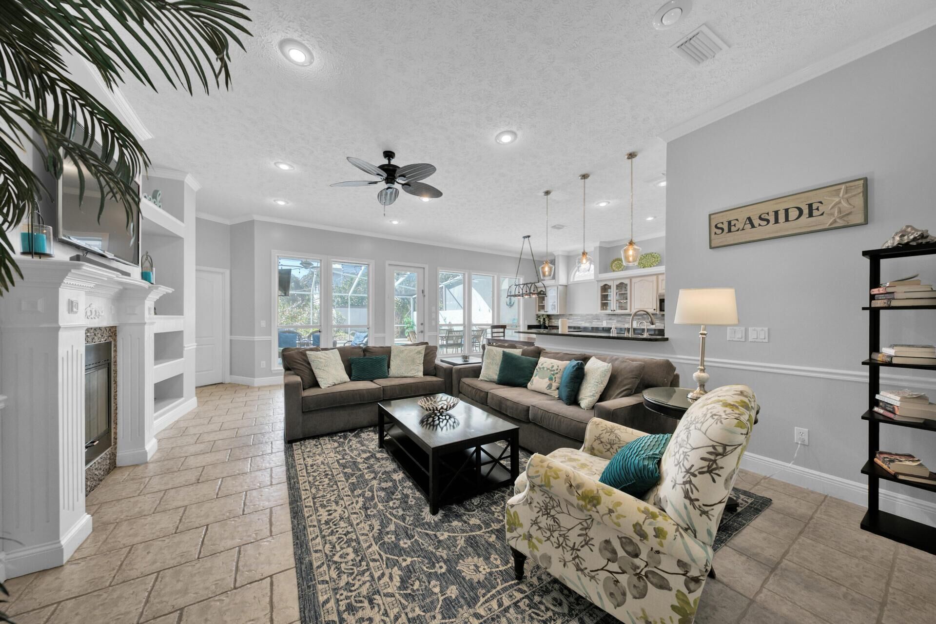 A spacious living room with a fireplace, a ceiling fan, and a view of the kitchen.