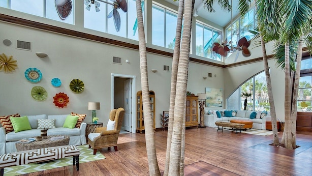 A spacious living area with high ceilings, large windows, and a view of palm trees. - Destiny Casa (Destin)