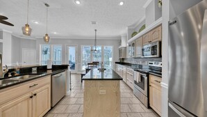 A modern kitchen with a central island, stainless steel appliances, and a view to the outdoors. - Destiny Casa (Destin)
