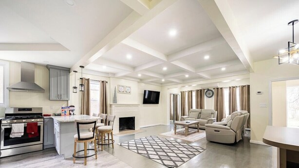 A modern kitchen with a built-in oven, a dining area with a table and chairs, a fireplace, and a living room with a sofa and a recliner.