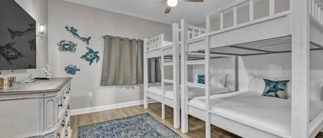 Una habitación con literas, ventilador de techo, decoración en la pared, cómoda y alfombra estampada.