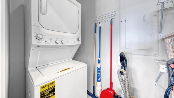 A laundry area with a white washing machine, two mops, and a red vacuum cleaner. - Shoreline Towers 2124 (Destin)
