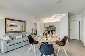 A modern living room with a sofa, dining table, chairs, a large mirror, and a kitchen in the background.
