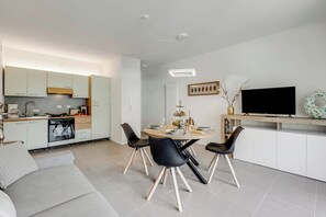 A modern kitchen with white cabinets, a dining area with a round table and four chairs, and a flat-screen TV mounted on the wall.