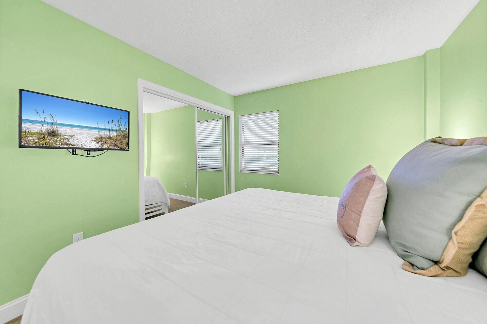 A bedroom with a large bed, a view of the beach through a window, and a door leading to a balcony.