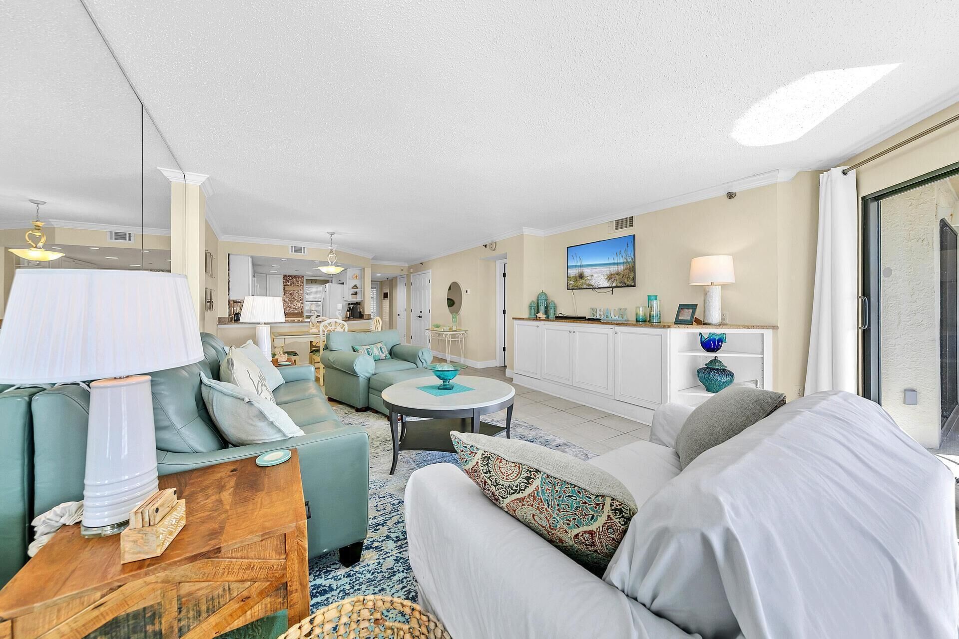 A spacious living room with a sofa set, a dining area, and a kitchen in the background.