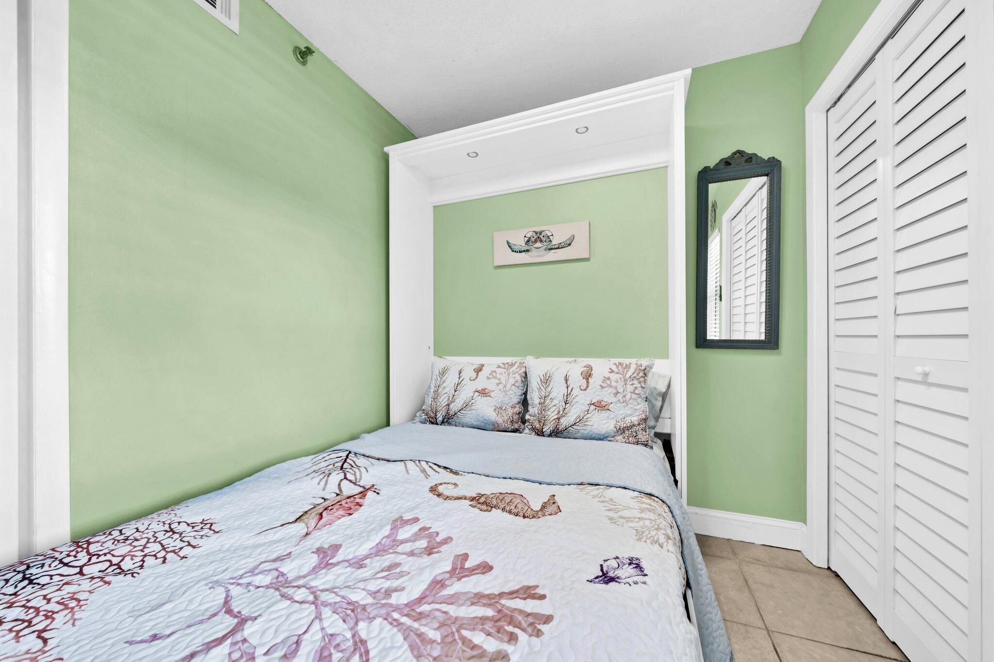 A bedroom with a bed, green walls, a white ceiling, a white door, and a mirror on the wall.