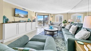 A spacious living room with a large flat-screen TV, a balcony with a view, and a cozy seating area with a green sofa and a coffee table. - Inlet Reef 215 (Destin)