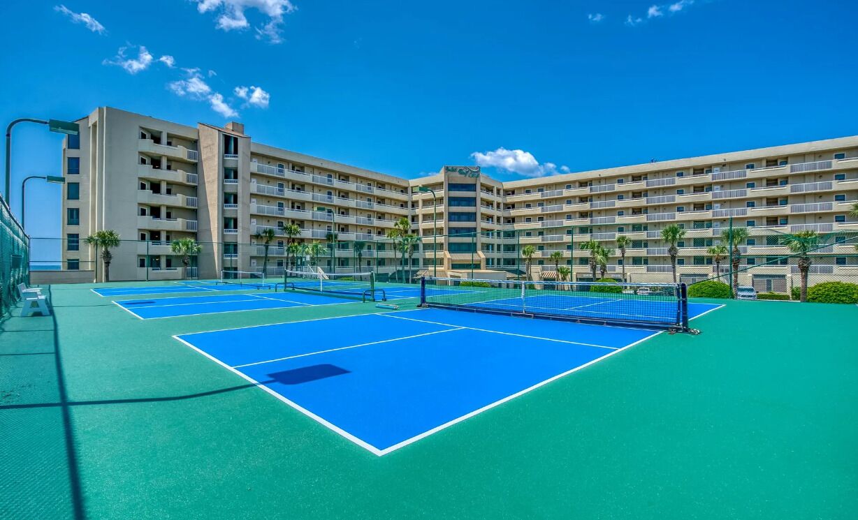 A tennis court with a net, surrounded by a multi-story hotel building with balconies.