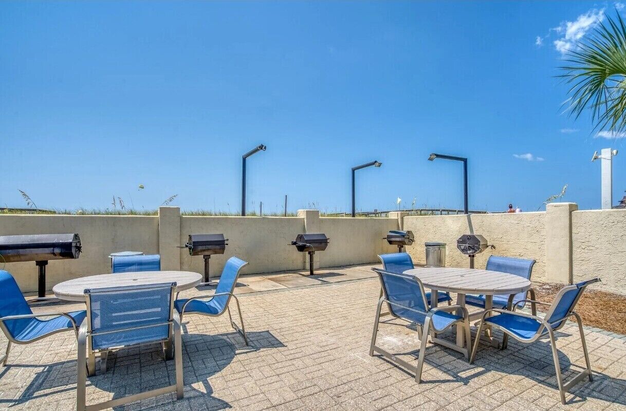 An outdoor patio with round tables and blue chairs, equipped with barbecue grills.