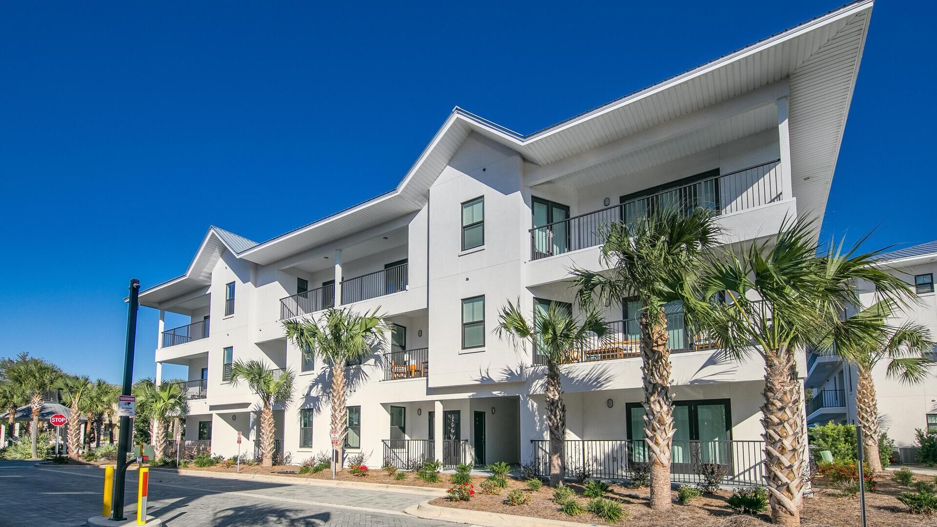 A modern multi-story building with balconies, palm trees, and a clear blue sky.