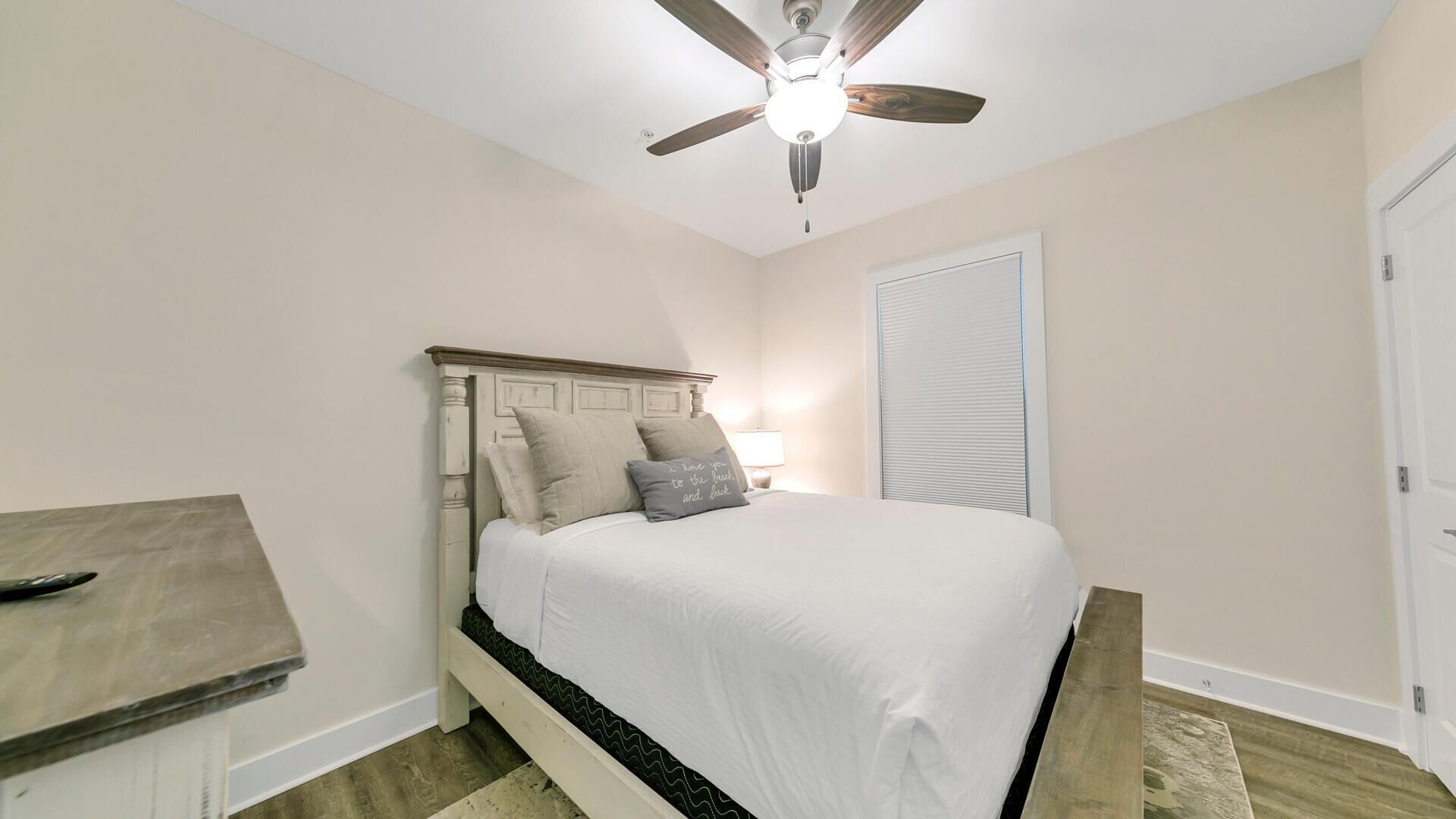 A bedroom with a bed, a ceiling fan, a bedside table, and a door.