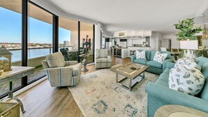 En rummelig stue med stort vindue der kigger ud over vand, et køkkenområde og en balkon med udsigt.