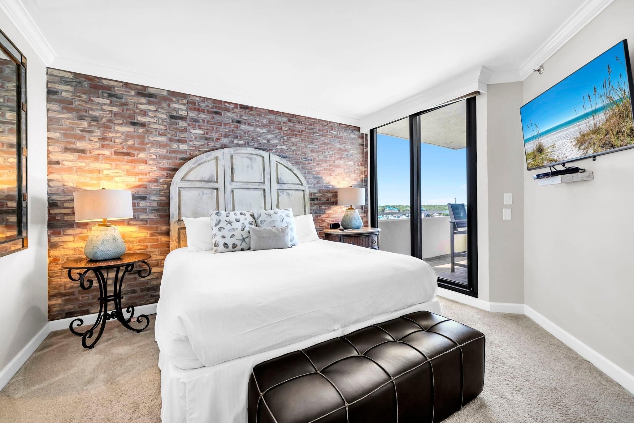 Un dormitorio con pared de ladrillo, una cama grande, un banco y vista a la playa.