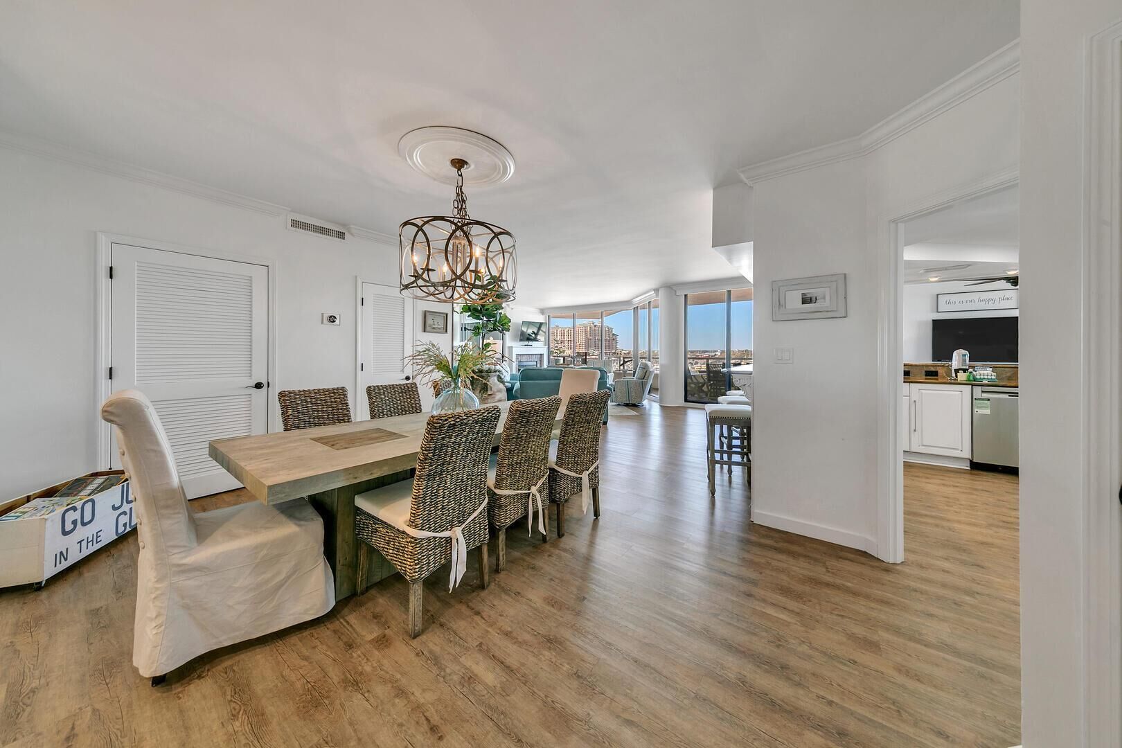 A dining area with a wooden table and wicker chairs, a chandelier, and a view of the city.