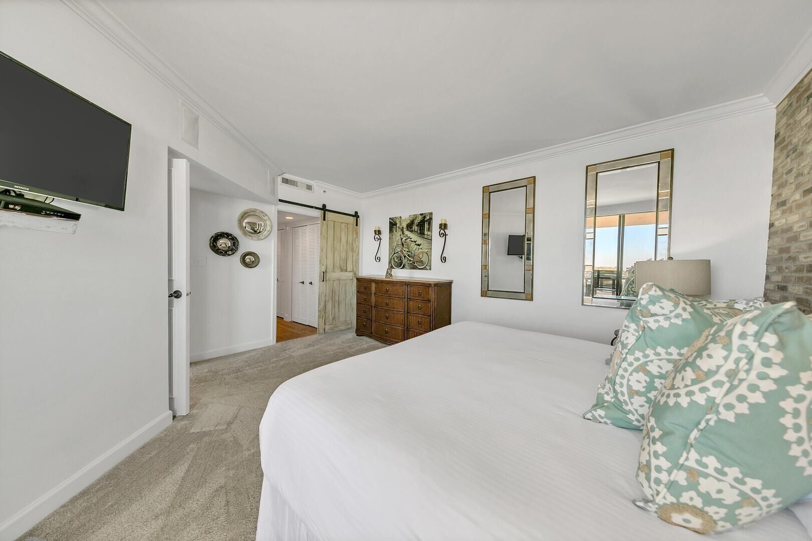 A bedroom with a large bed, a dresser, a mirror, and a television mounted on the wall.