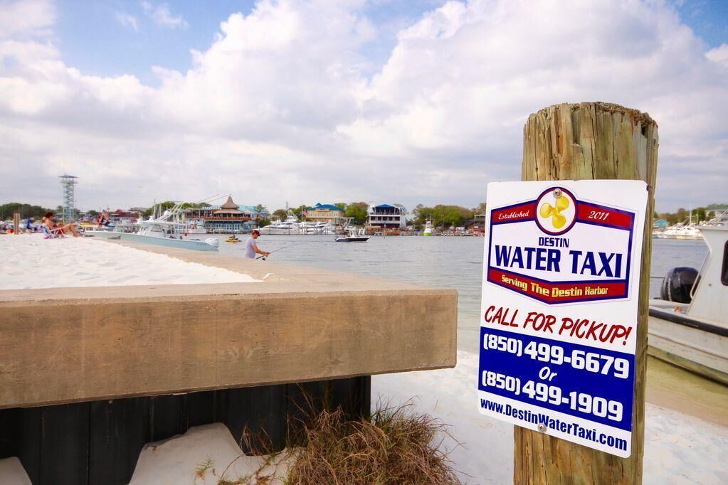 A waterfront area with a sign for Destin Water Taxi, established in 2011, offering pickup services.