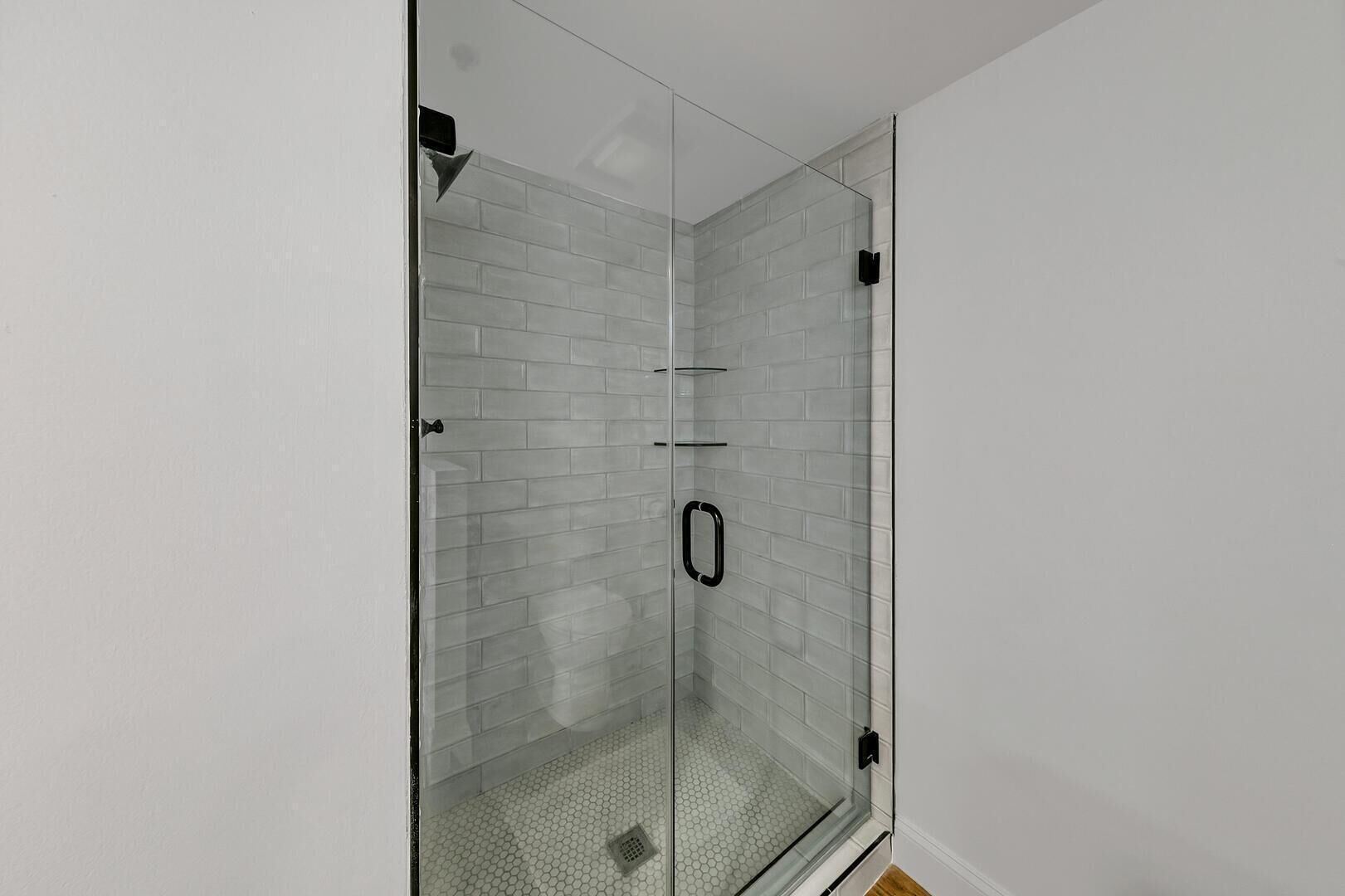 Una ducha con cerramiento de vidrio, pared con azulejos blancos y un grifo negro.