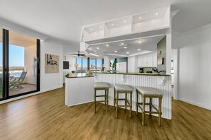 A modern kitchen with a central island, bar stools, and a view of the sea through large sliding doors. - East Pass Towers 603 (Destin)