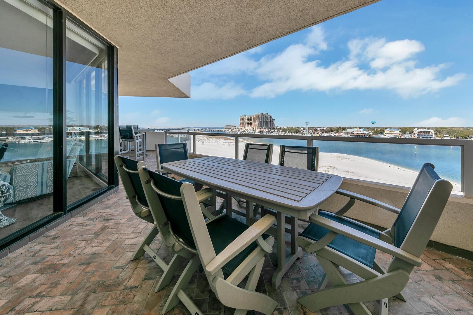 A balcony with a table and chairs overlooking a beach and marina.