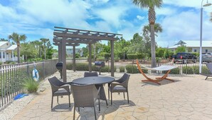 An outdoor patio with a pergola, a round table with chairs, a hammock, and a grill. - Once Upon a Tide (Santa Rosa Beach)