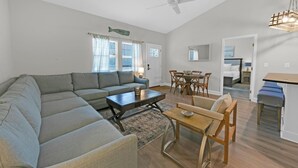 A modern living room with a sectional sofa, a coffee table, and a dining area with a table and chairs. - Once Upon a Tide (Santa Rosa Beach)