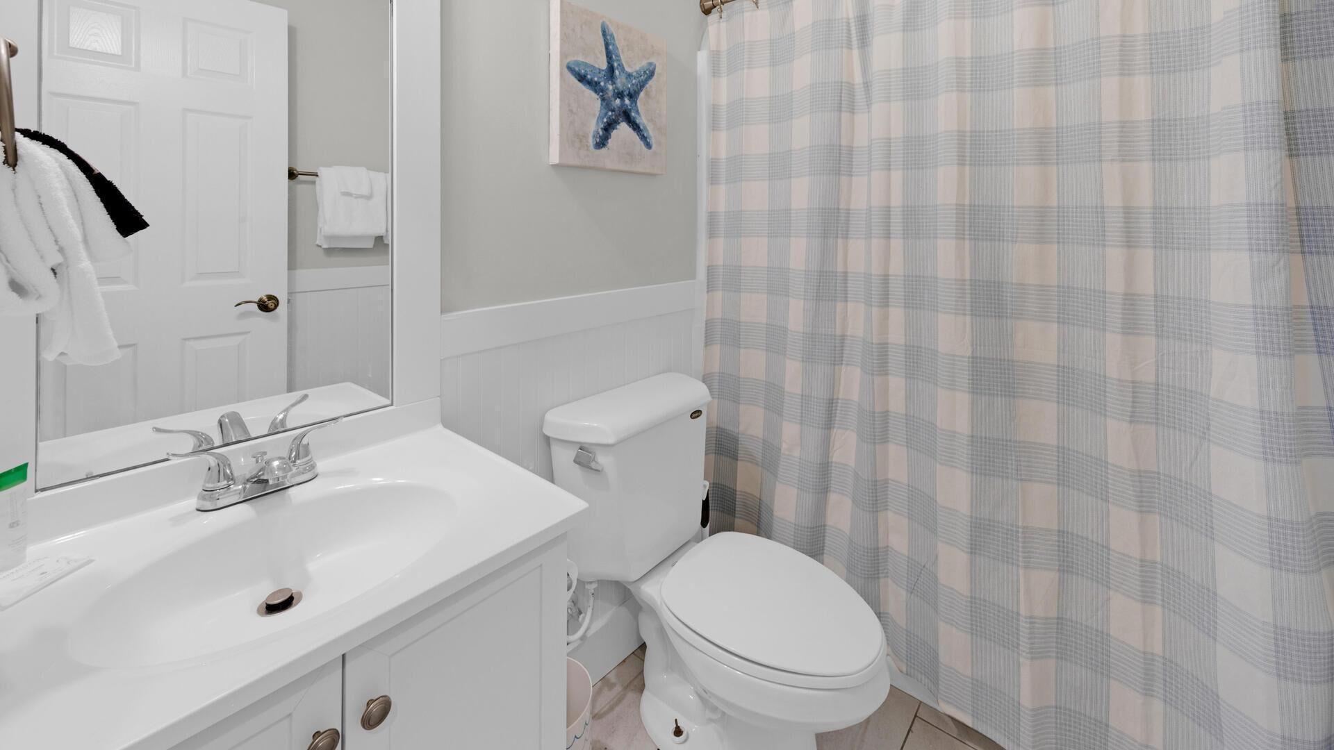 A bathroom with a white sink, toilet, and a plaid shower curtain.