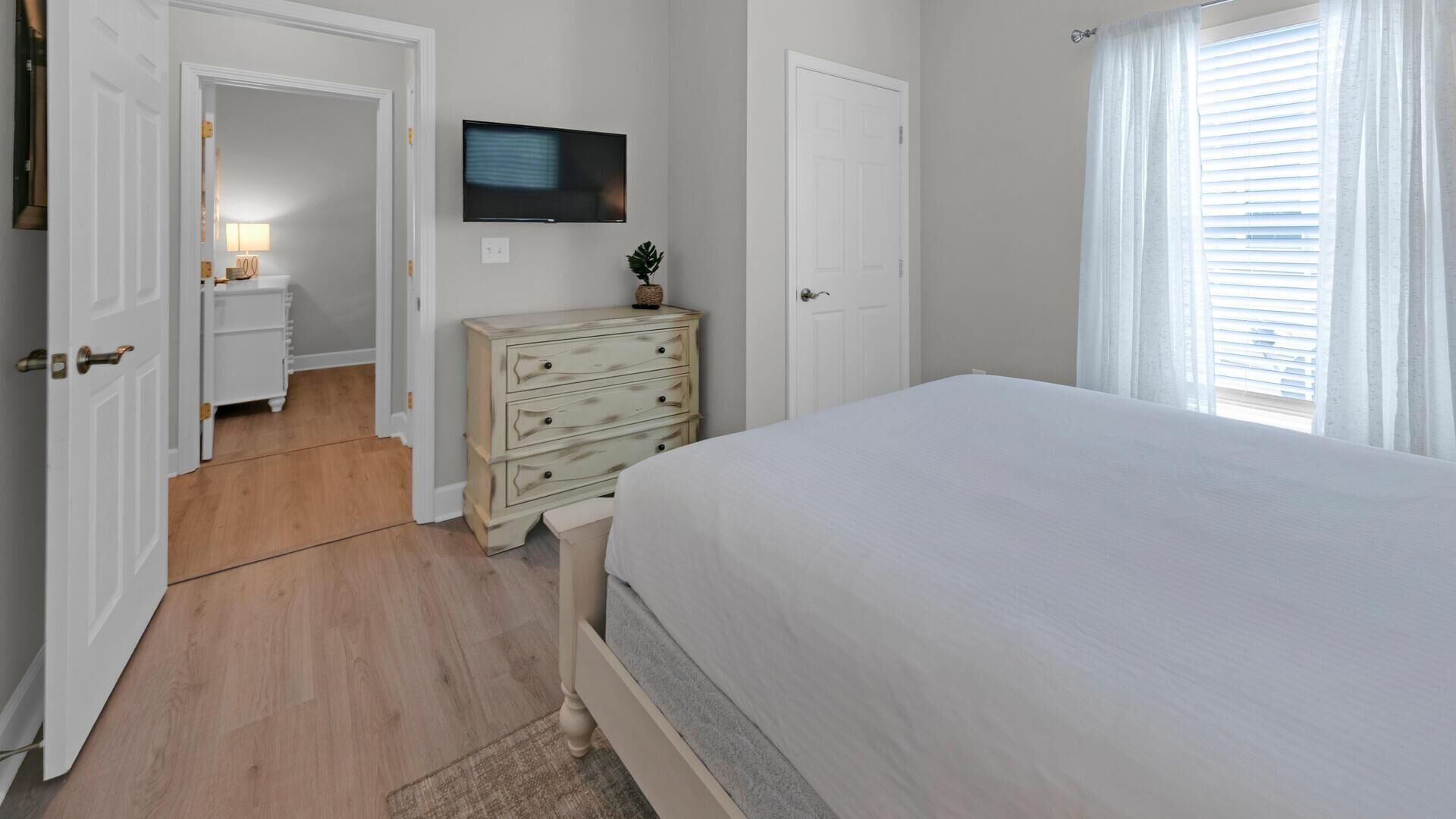 A bedroom with a bed, a dresser, a television, and a door leading to another room.