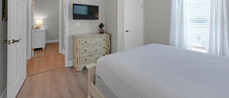 A bedroom with a bed, a dresser, a television, and a door leading to another room.